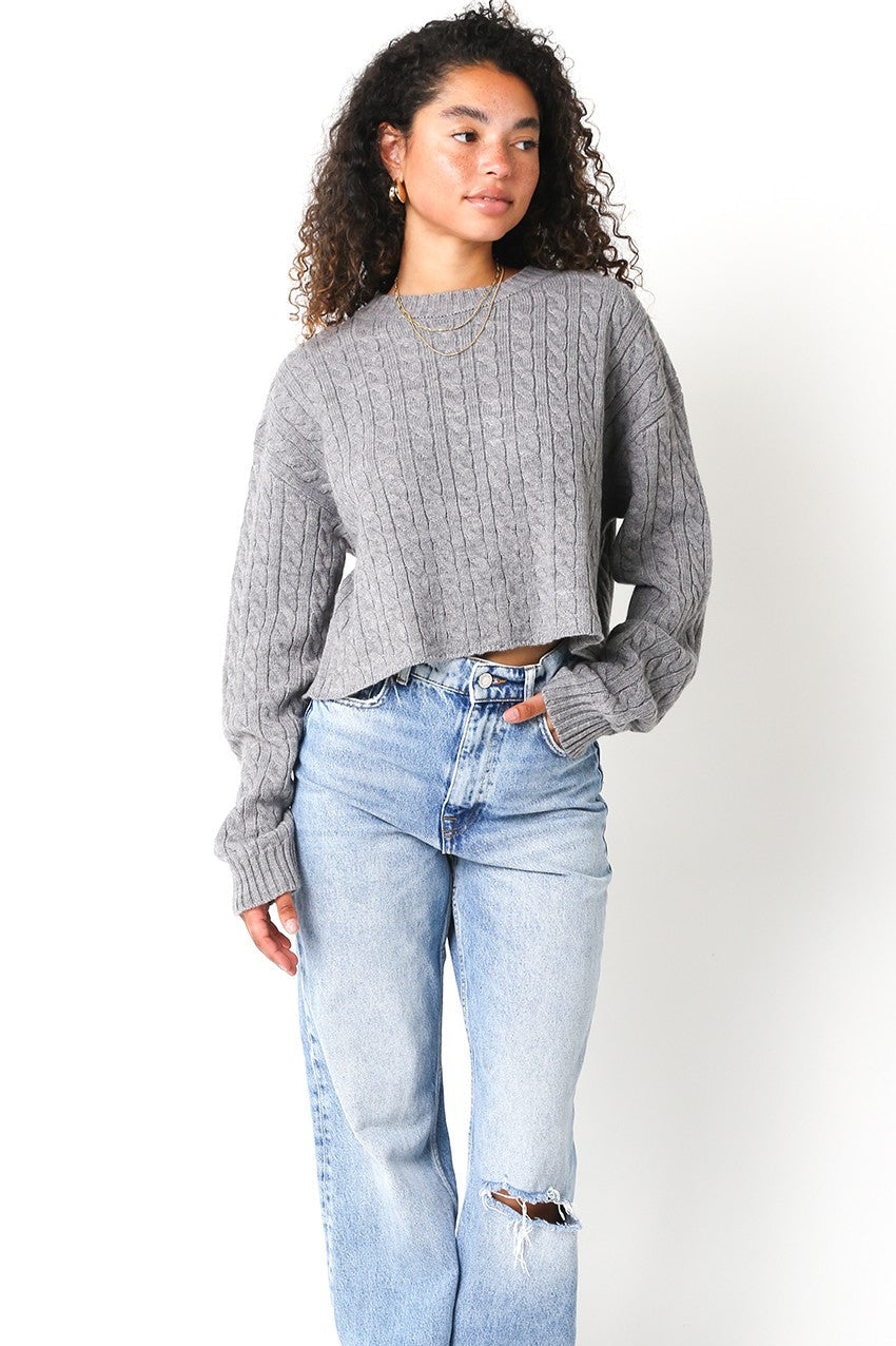 Woman wearing a gray sweater and light blue jeans on a white background