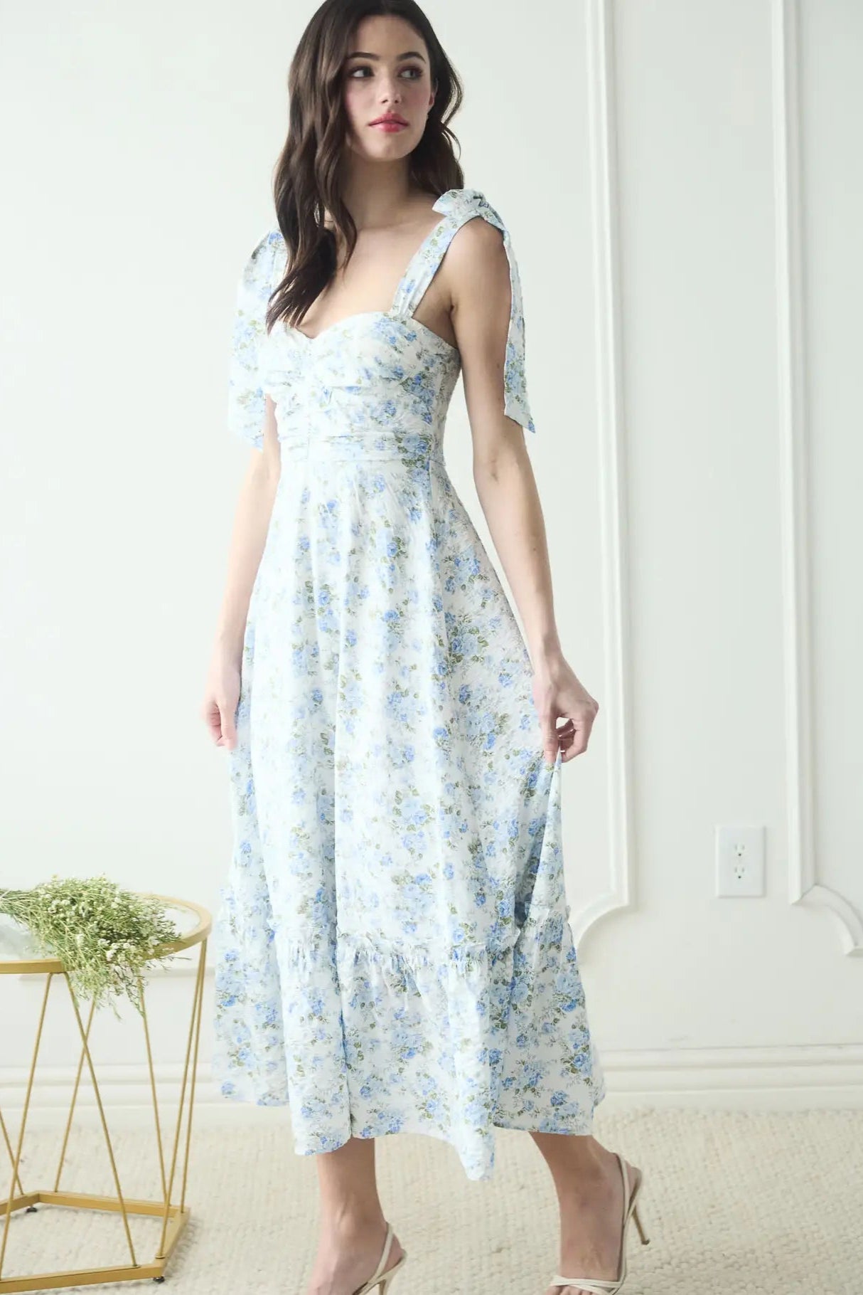 Woman in a floral dress standing in a minimalistic room.