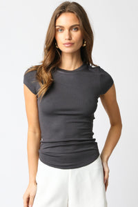 Woman wearing a dark gray t-shirt and white pants on a light gray background