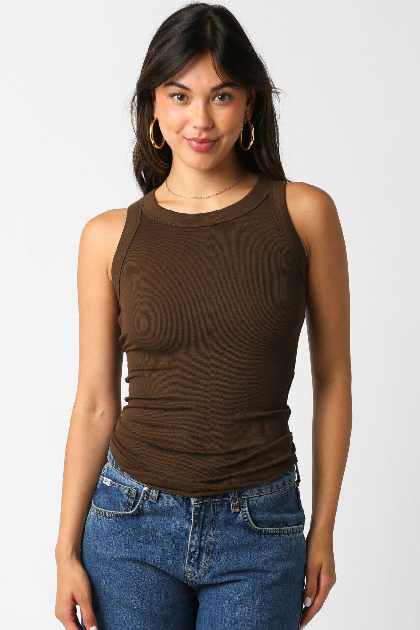 Woman wearing a brown tank top and blue jeans against a white background