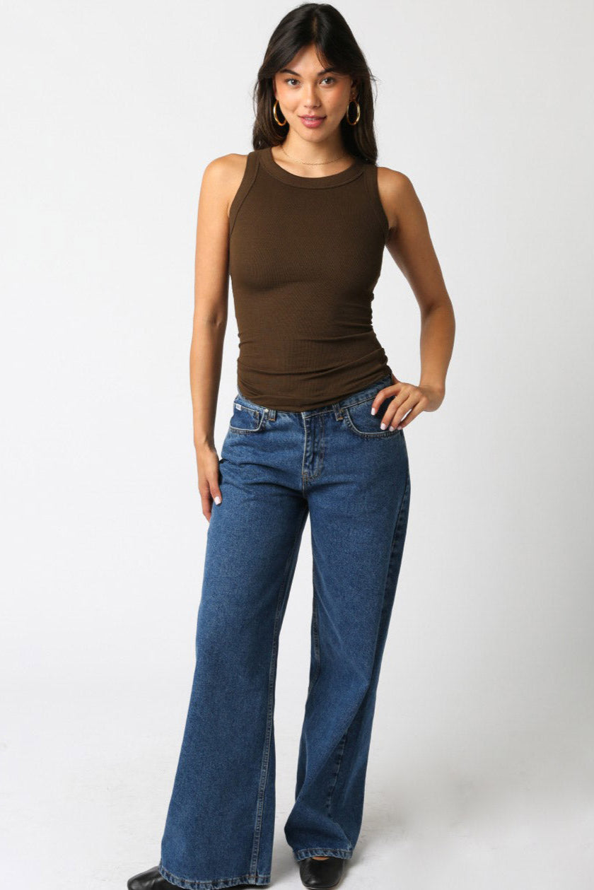 Woman wearing a brown tank top and blue jeans on a white background