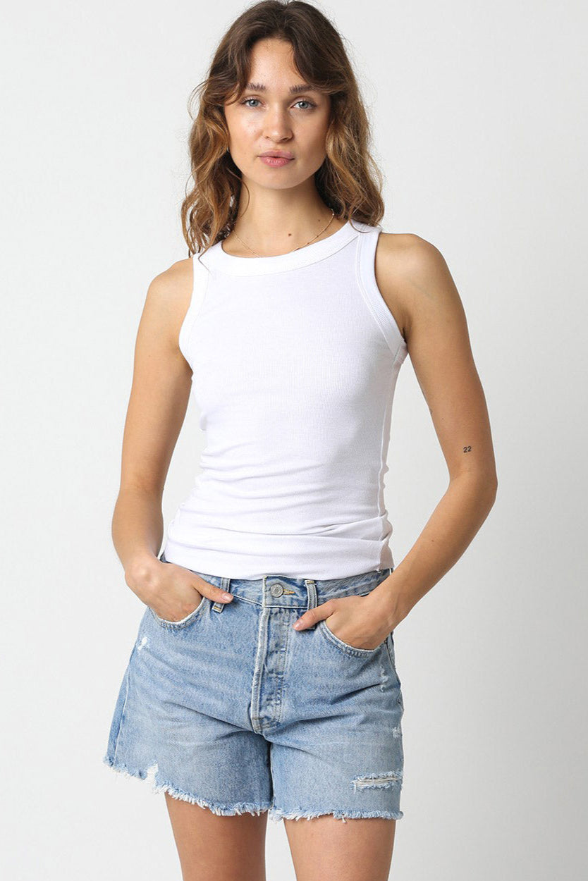 Woman wearing a white tank top and denim shorts on a plain background