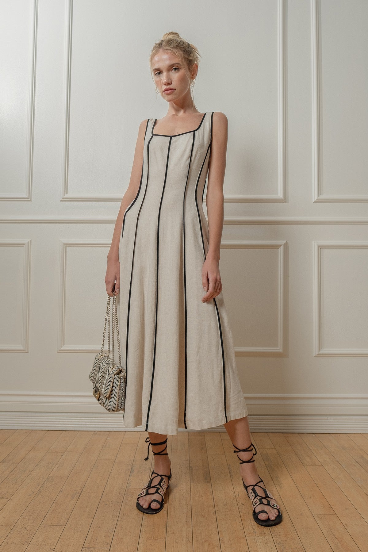 Woman wearing a white dress with black stripes against a white paneled wall.