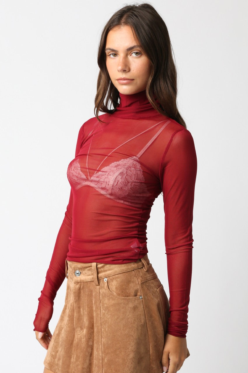Woman wearing a red turtleneck with a sheer overlay and a brown skirt on a white background