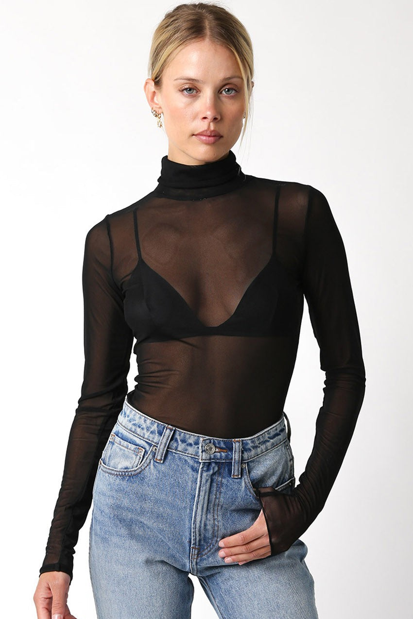 Woman wearing a black sheer long-sleeve top and blue jeans on a white background