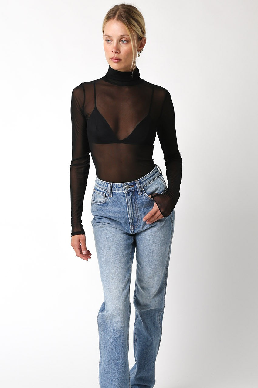 Person wearing a sheer black top and blue jeans on a white background