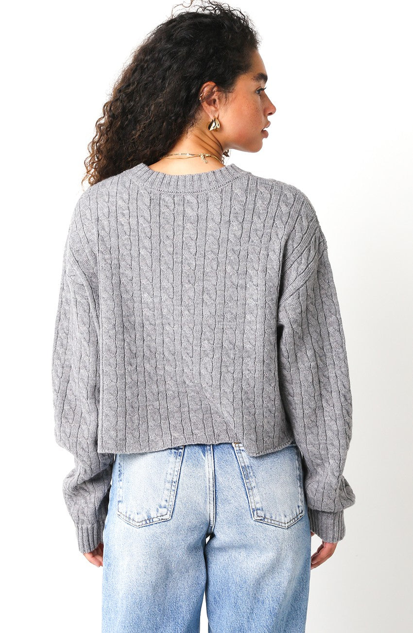 Person wearing a gray cable knit sweater and light blue jeans on a white background