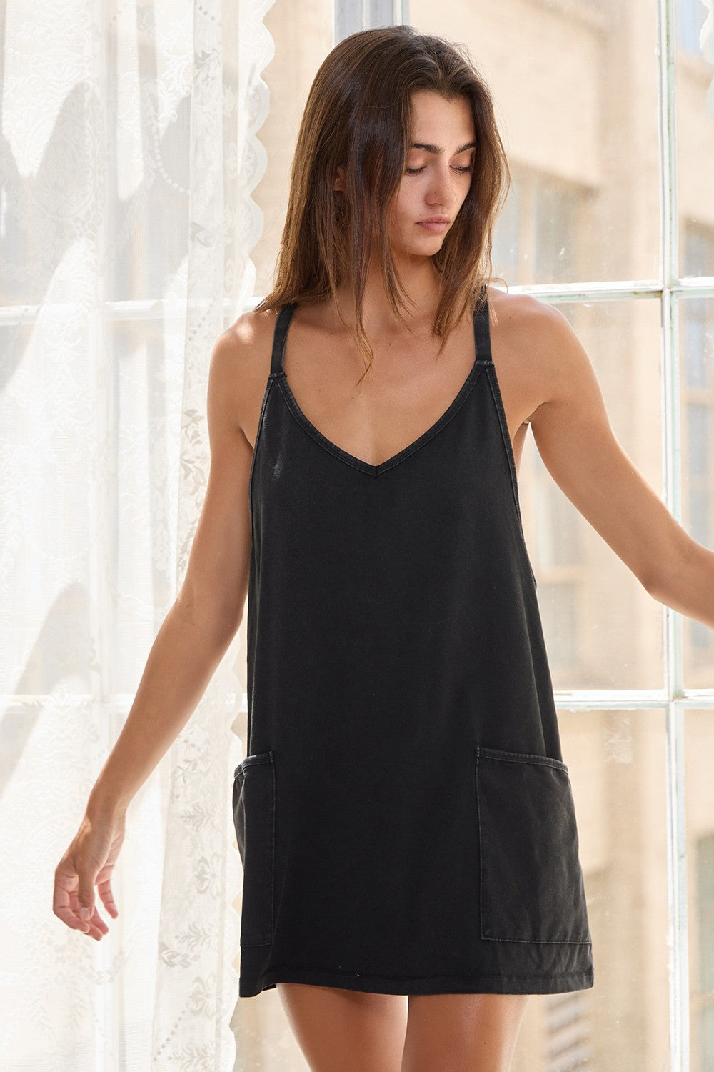 Woman wearing a black sleeveless dress standing in a softly lit room.