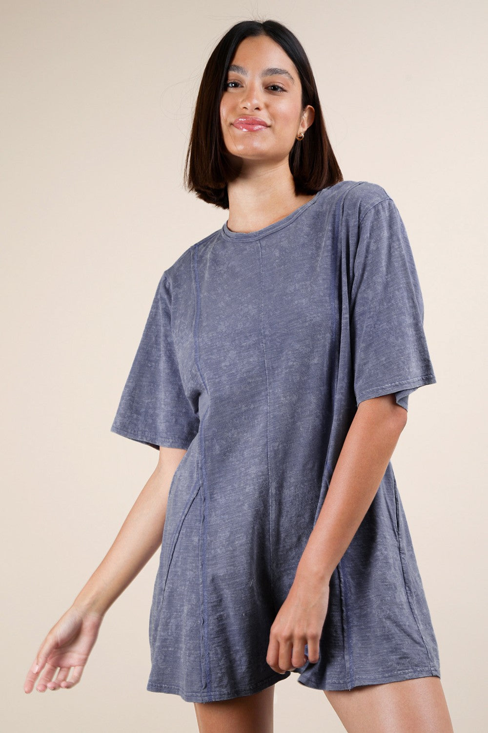 A woman wearing a gray relaxed fit romper with a round neck, short sleeves, and raw edge details.
