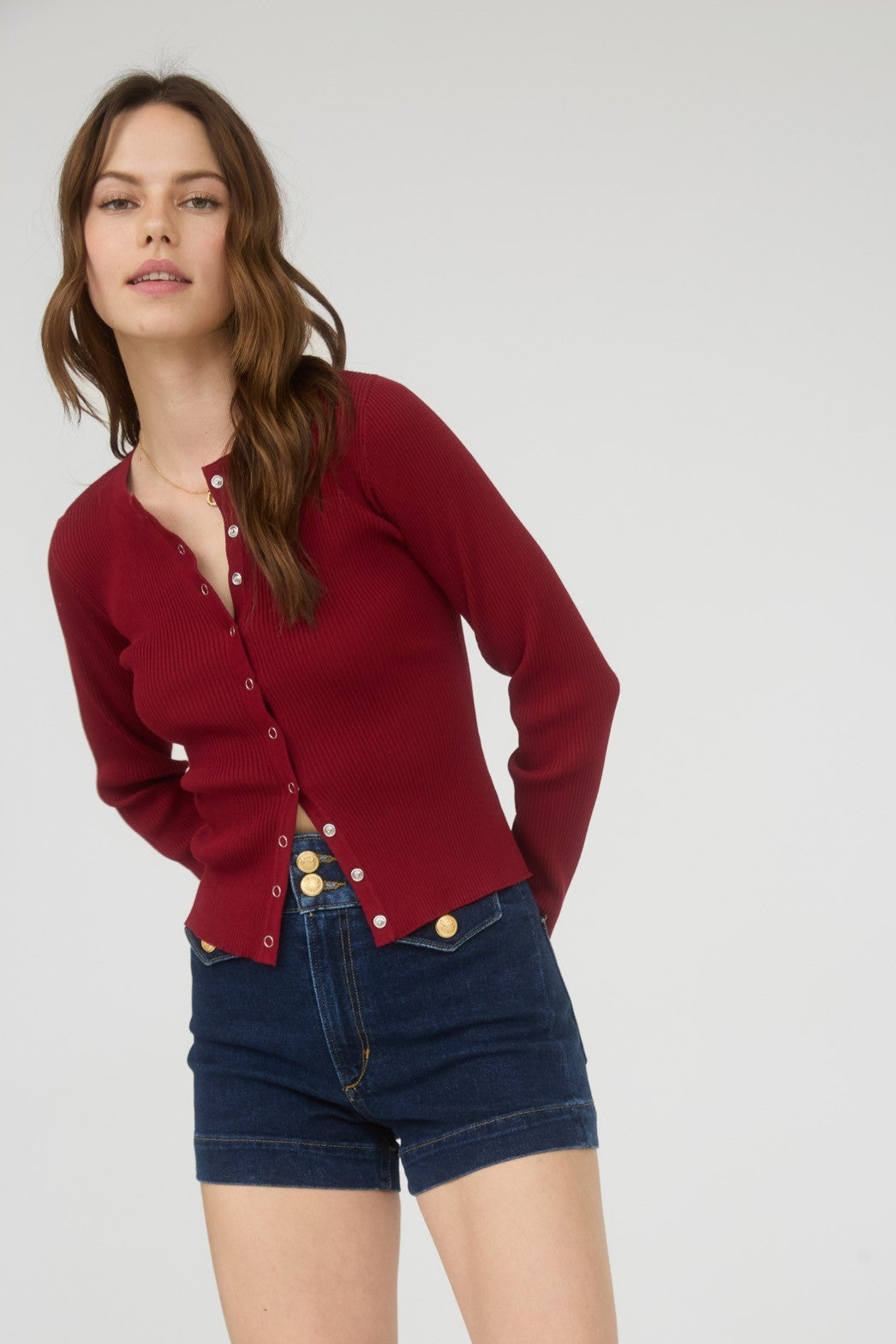 Woman wearing a red cardigan, blue shorts, and brown boots on a white background