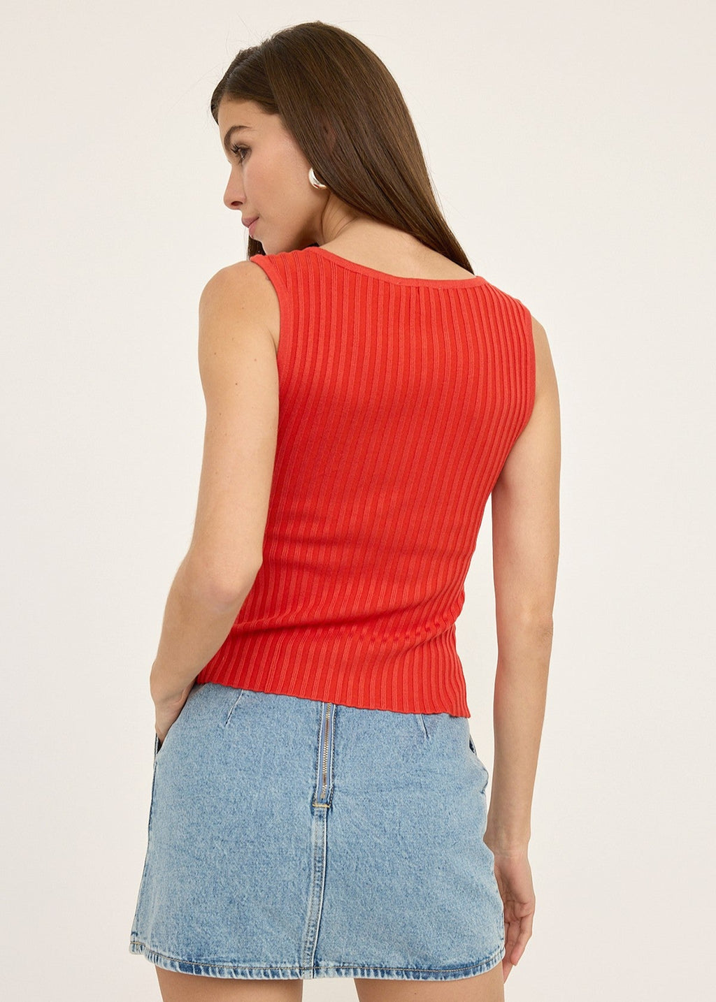 Woman wearing a red sleeveless top and denim skirt on a plain background