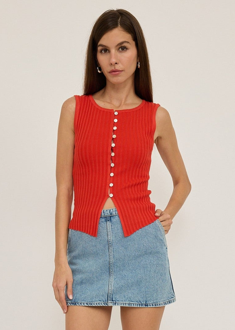 Woman wearing a red sleeveless top and denim skirt on a plain background