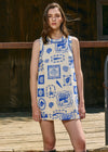 Woman wearing a sleeveless dress with blue patterns standing outdoors.