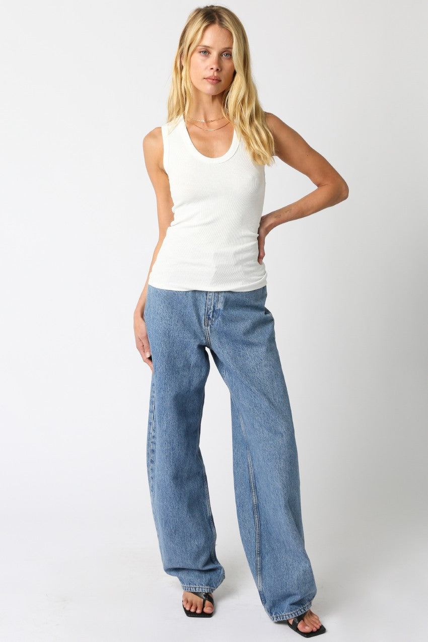 Woman wearing a white tank top and blue jeans on a white background