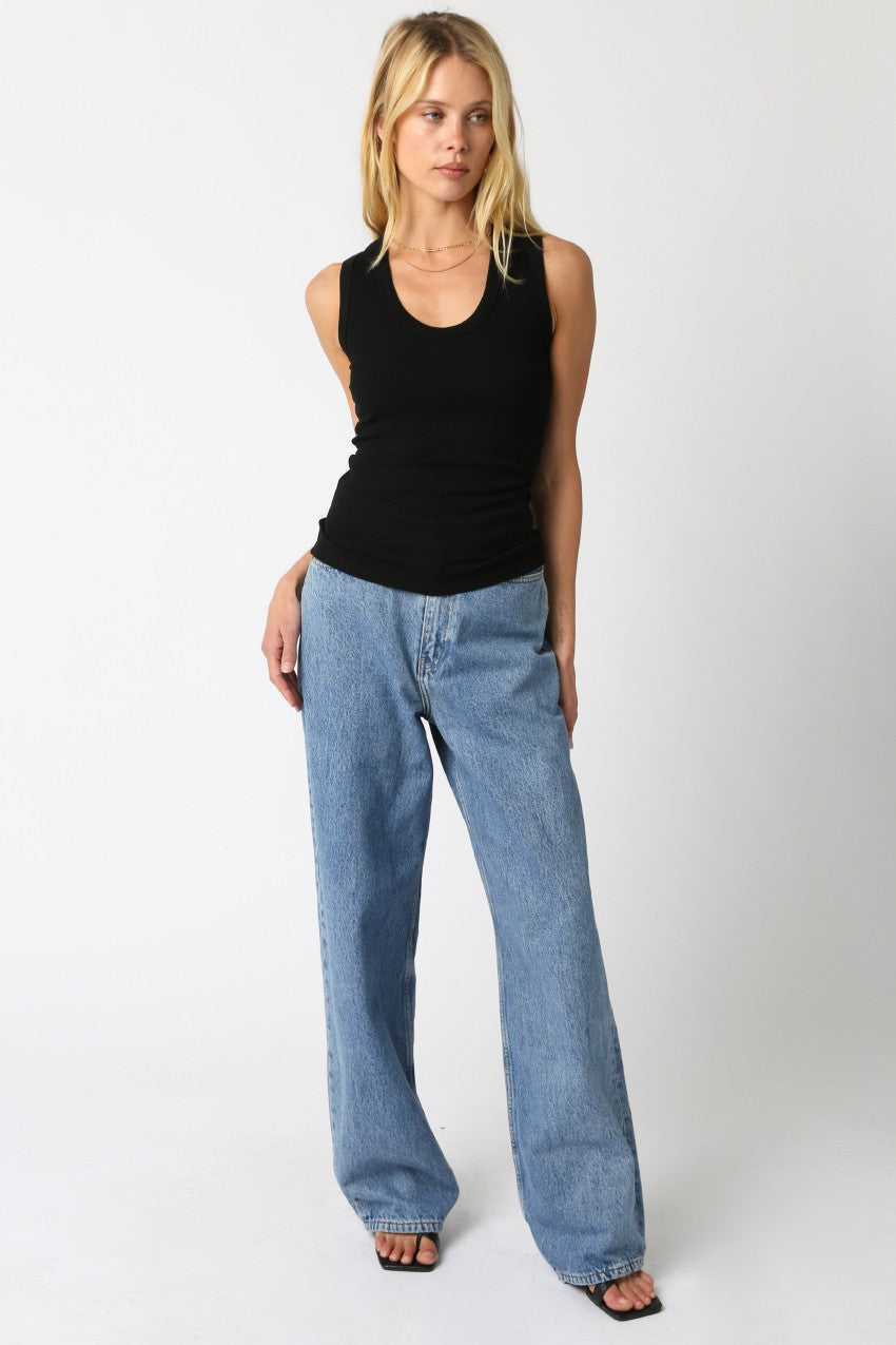 Woman wearing a black tank top and blue jeans on a white background