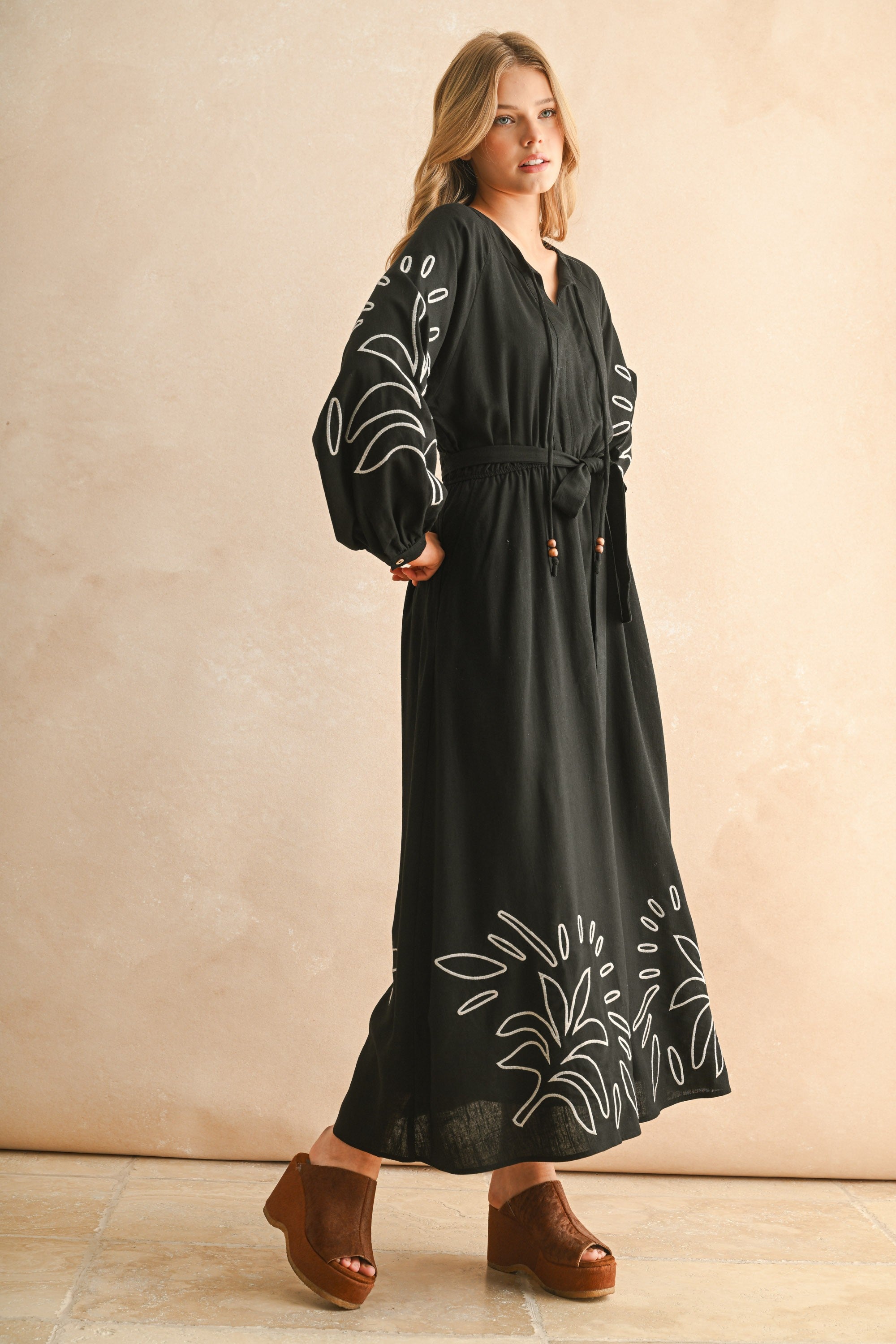 Woman wearing a black dress with white embroidery against a beige background