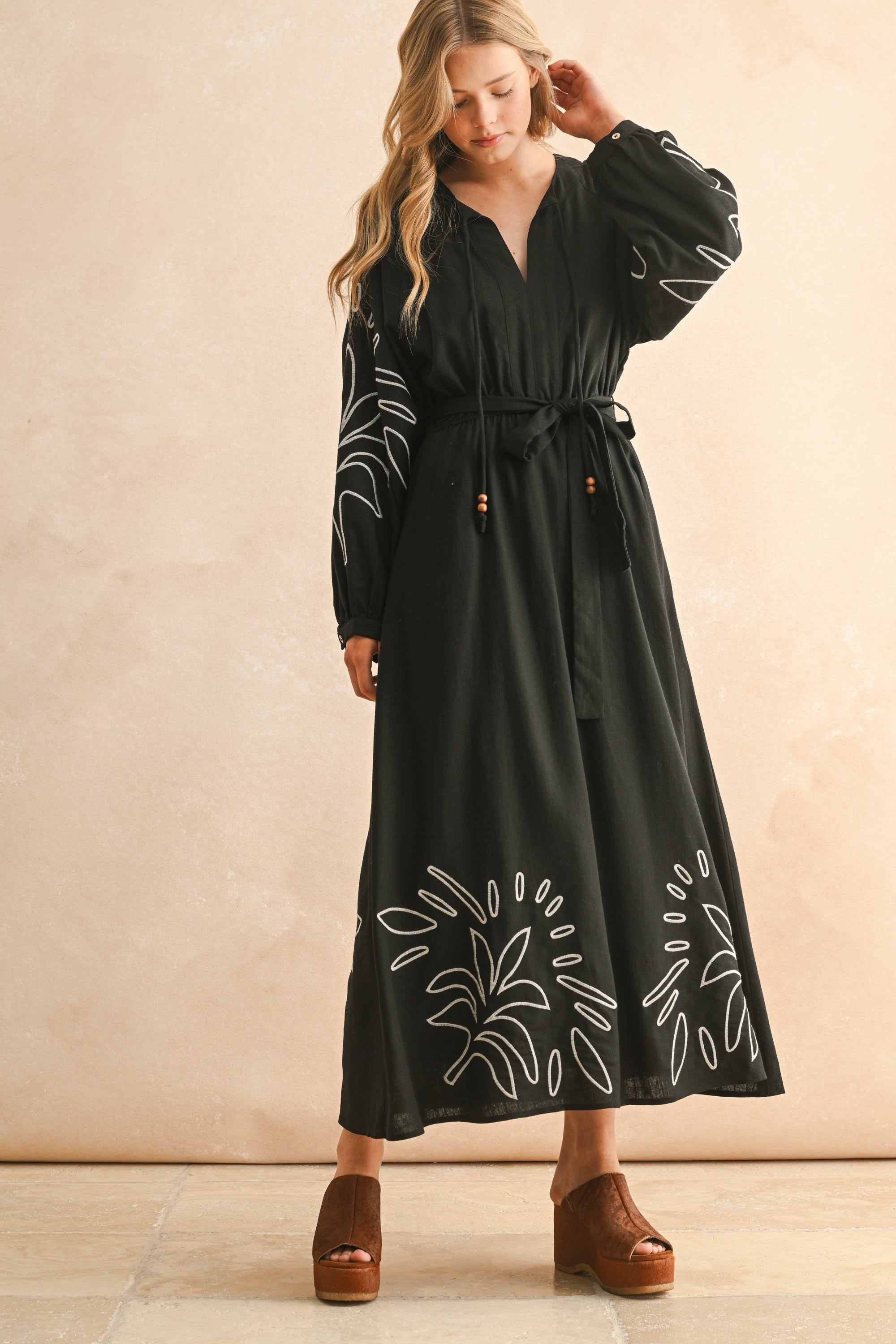 Woman wearing a black dress with white floral embroidery on a beige background