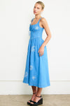 Woman wearing a blue dress with white floral embroidery against a white background