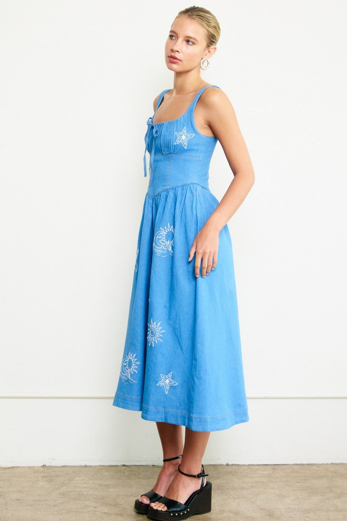 Woman wearing a blue dress with white floral embroidery against a white background
