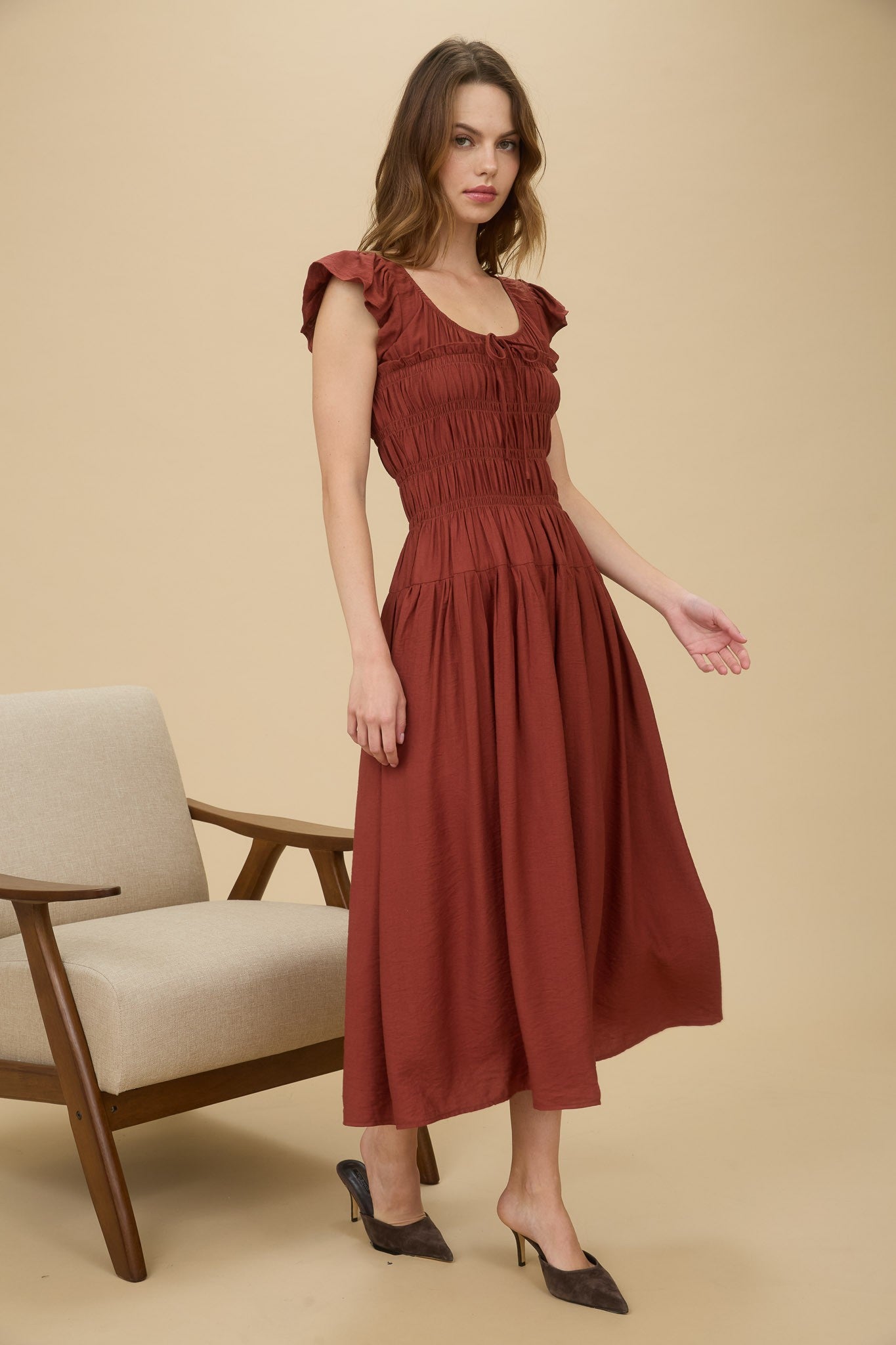 Woman wearing a rust-colored dress standing against a beige background