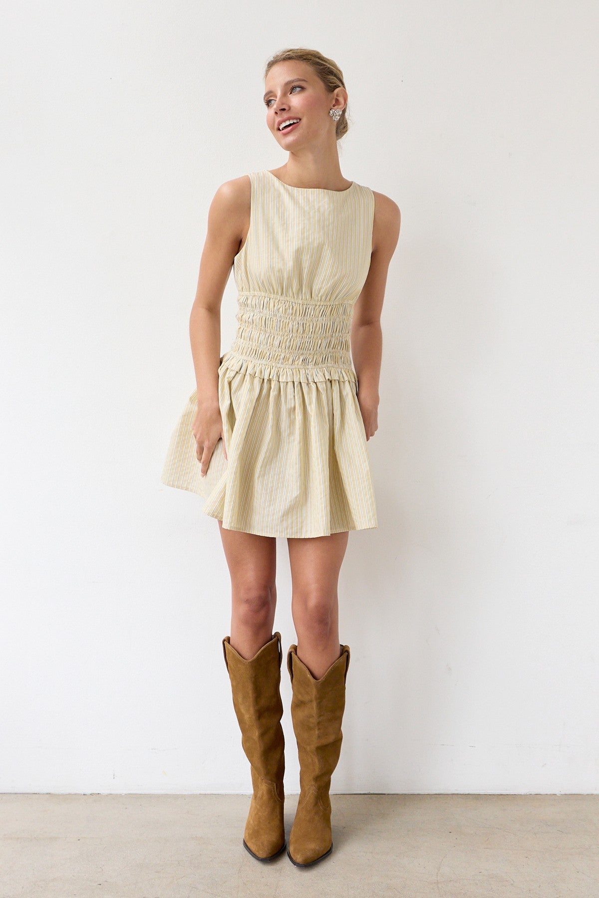Woman wearing a light-colored dress and brown knee-high boots against a white background