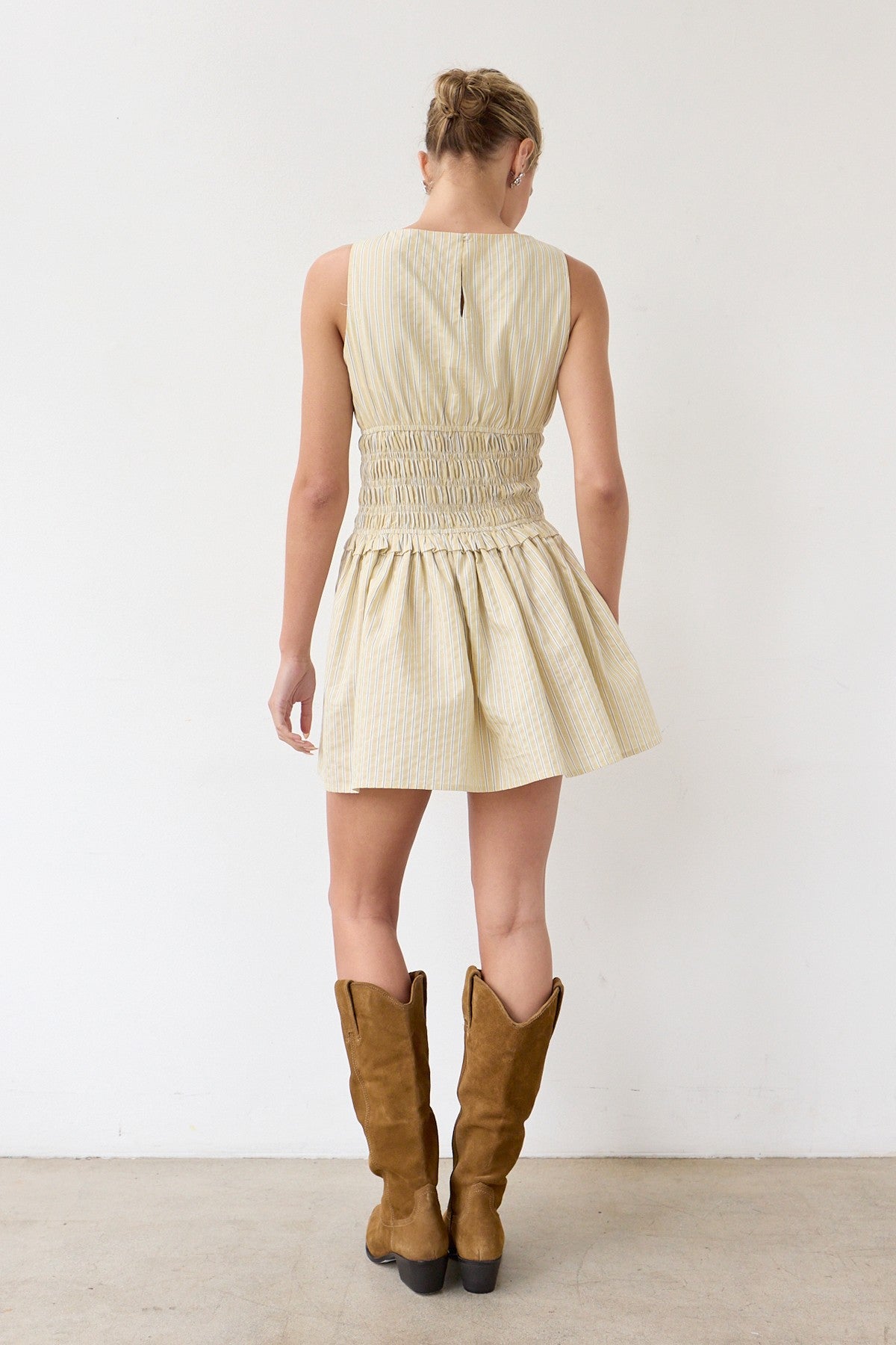 Woman wearing a beige dress and brown boots against a white background