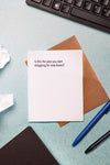 Note card with humorous text on a desk with crumpled paper and pens.