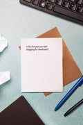 Note card with humorous text on a desk with crumpled paper and pens.