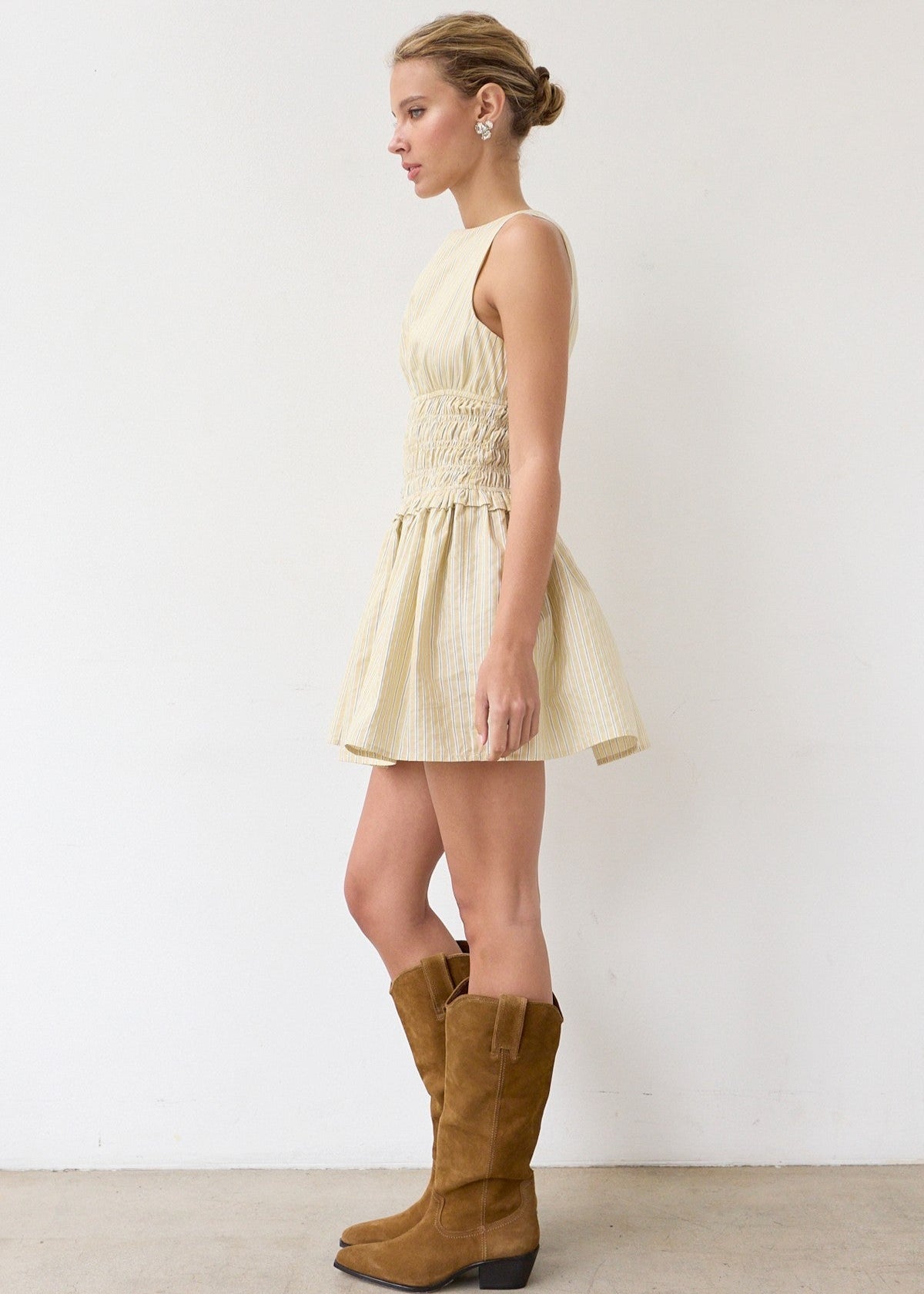 Woman wearing a light-colored dress and brown knee-high boots against a white background