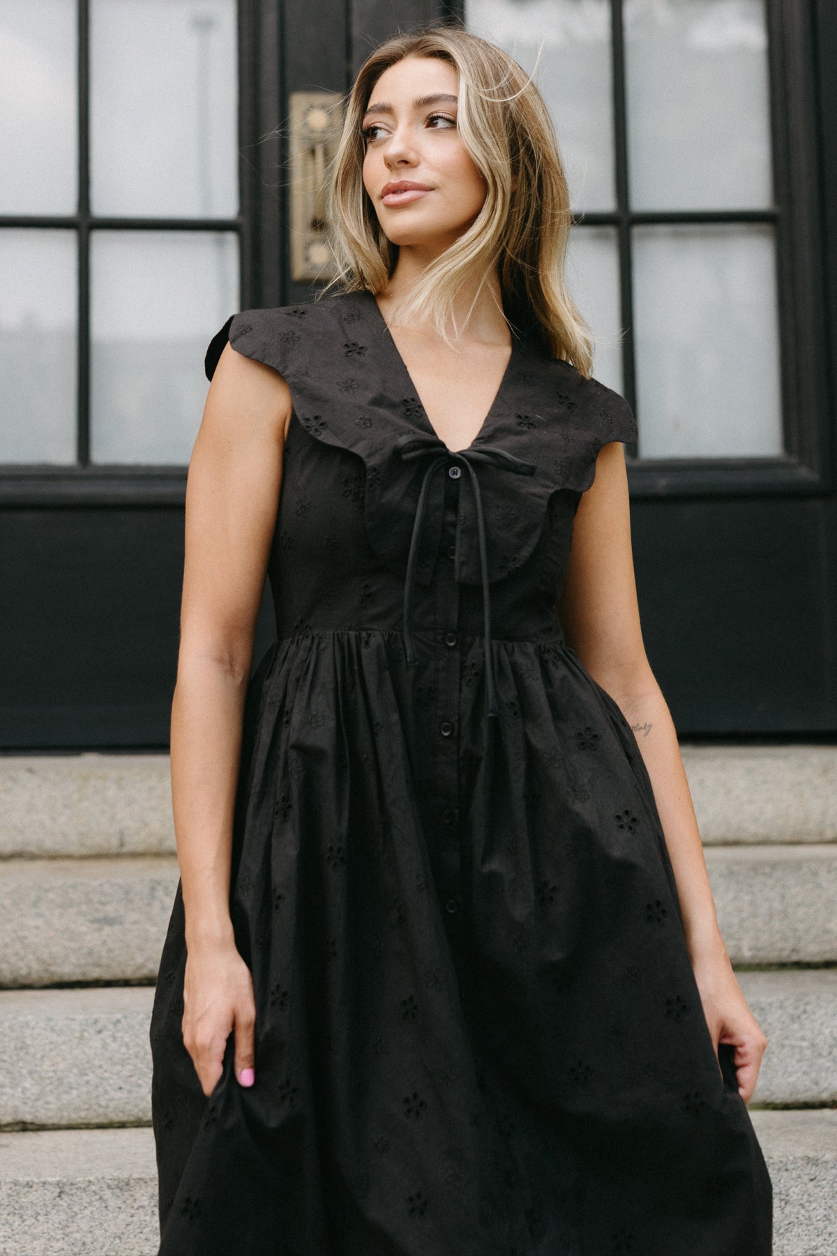 Woman wearing a black dress standing on steps with a blurred background