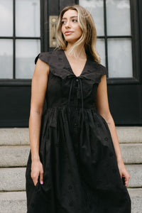 Woman wearing a black dress standing on steps with a blurred background