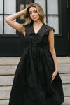 Woman wearing a black dress standing on steps in front of a black door.
