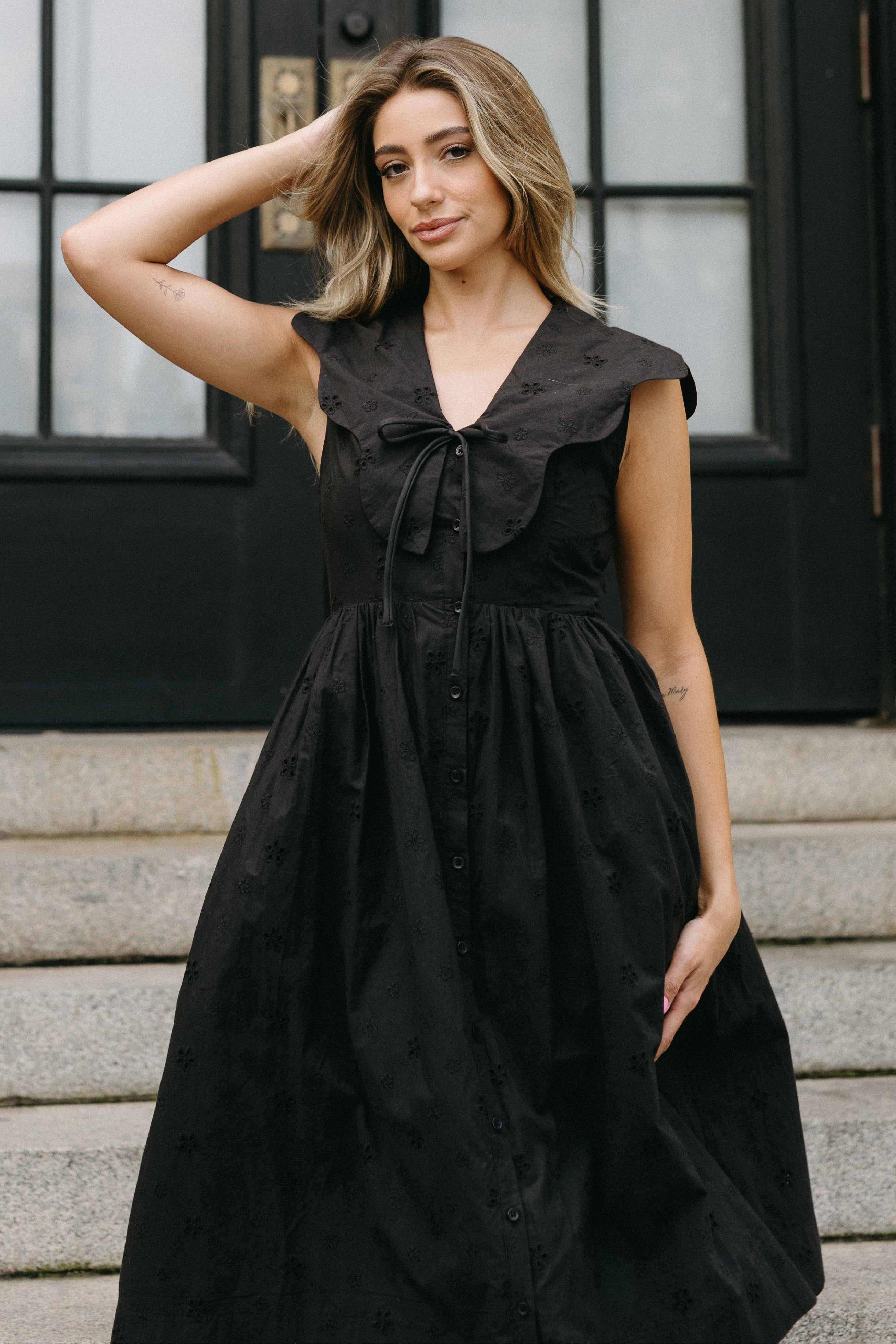 Woman wearing a black dress standing on steps in front of a black door.