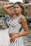 Woman in a striped outfit standing by a waterfront with boats and buildings in the background