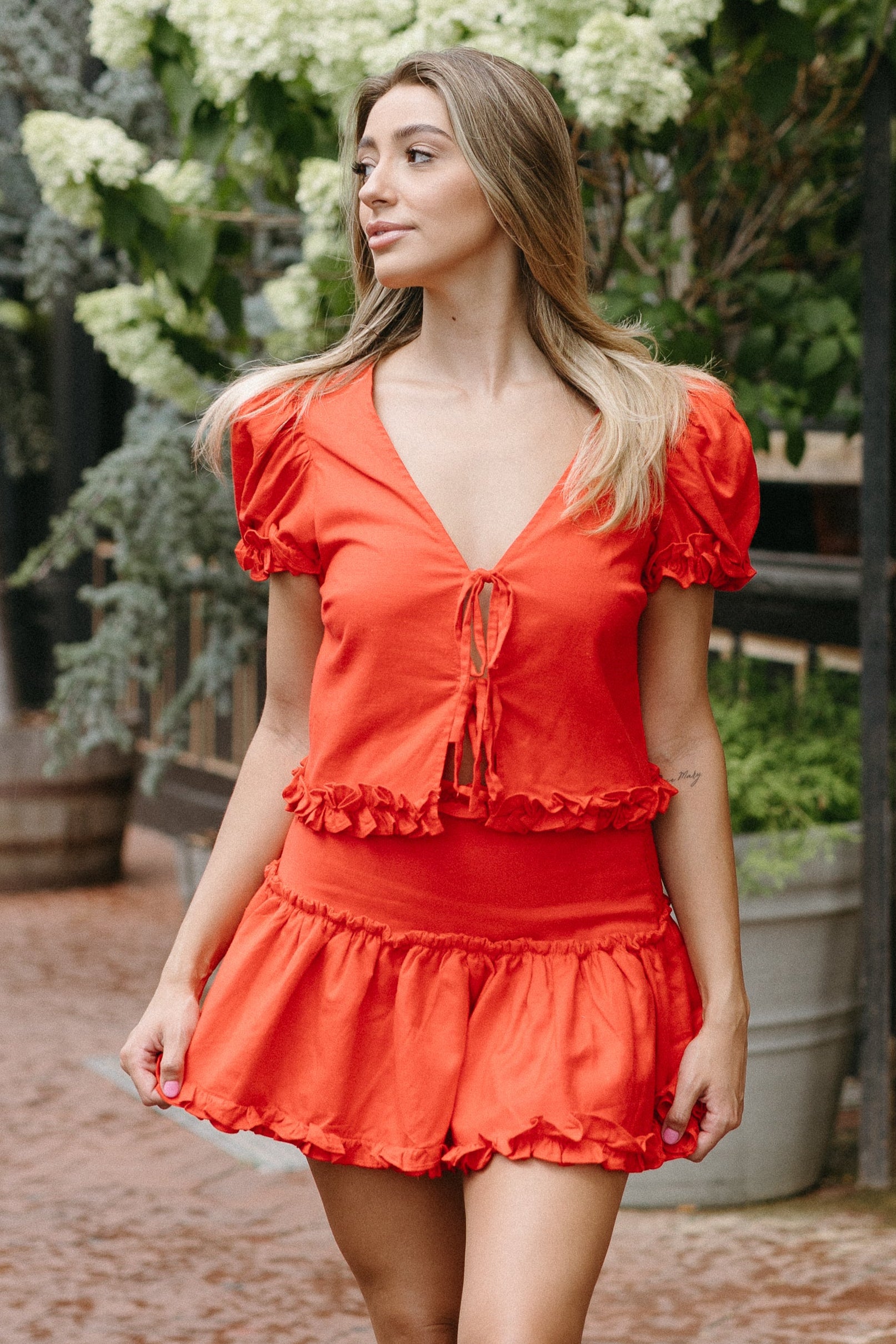 Woman in a red dress walking on a brick path with floral decorations and a brick building in the background.
