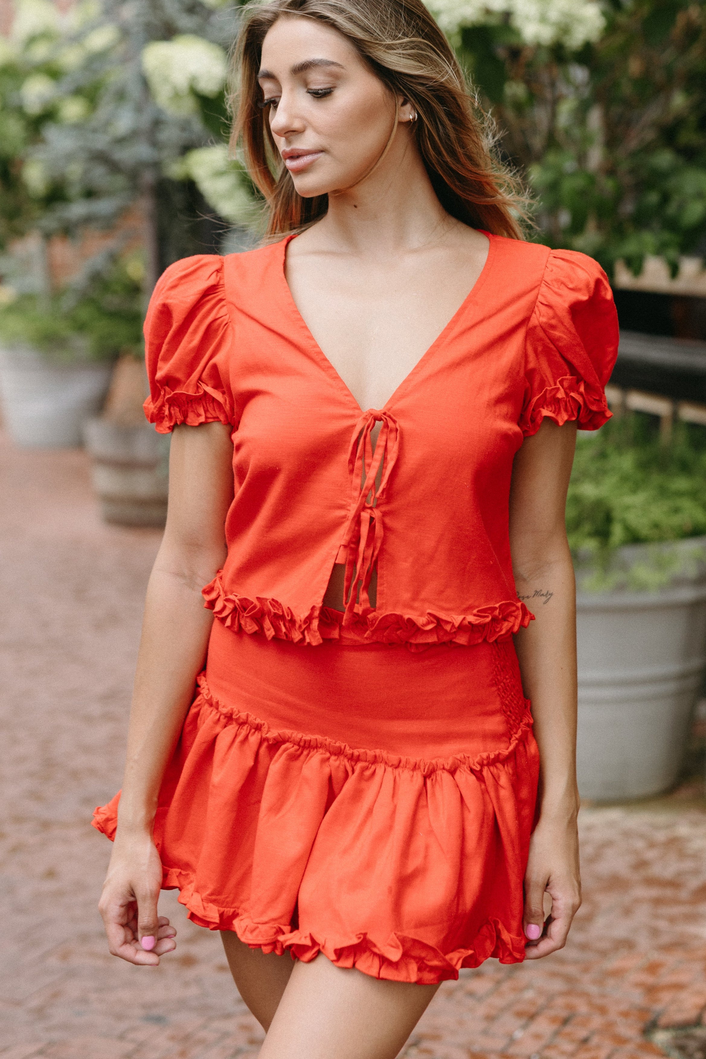 Woman wearing a red dress standing outdoors with plants and flowers in the background