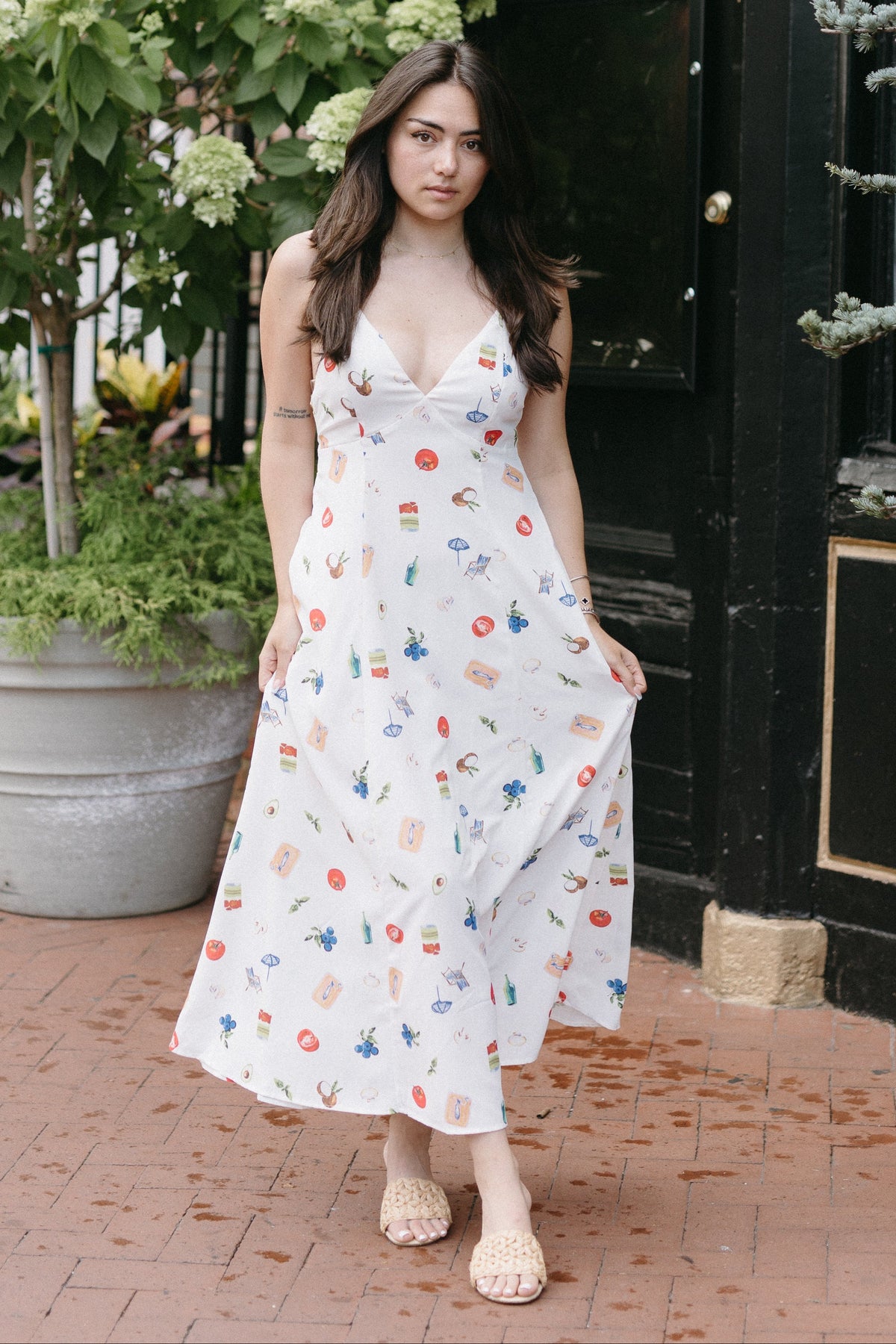 Woman in a floral dress standing in front of a building with plants around.