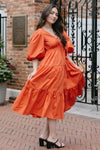 Woman in an orange dress standing in front of a brick building with decorative elements.