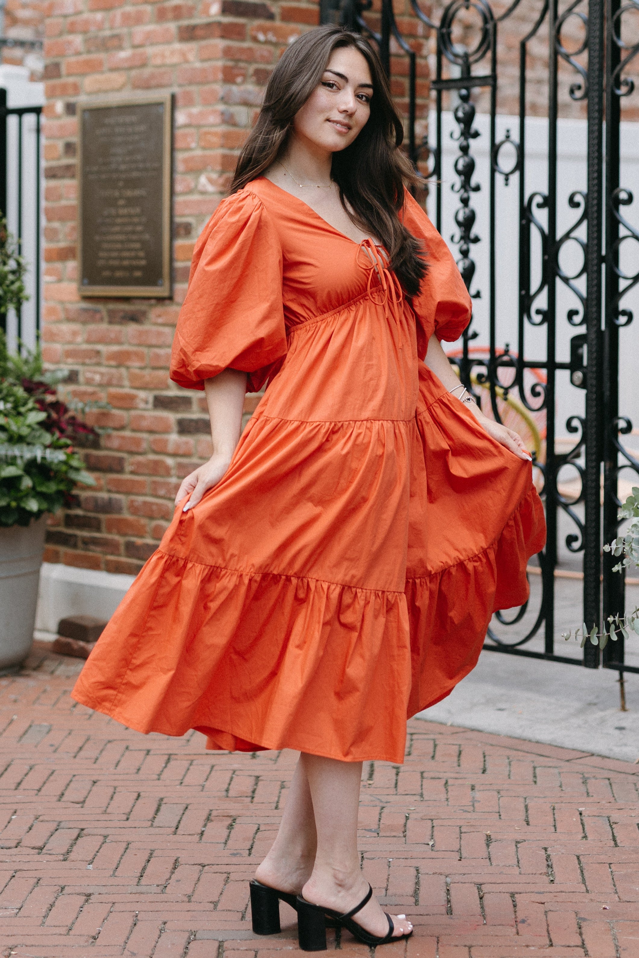 Woman in an orange dress standing in front of a brick building with decorative elements.