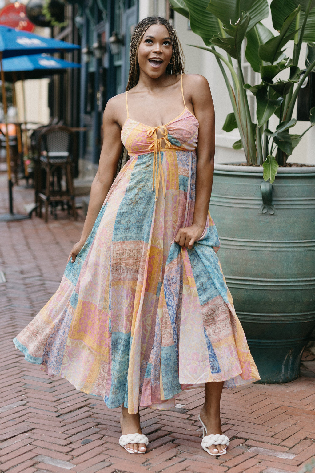 Woman in a colorful dress standing on a street with plants and buildings in the background