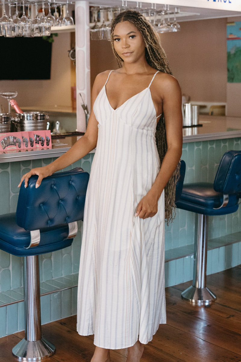 Woman in a white dress standing in a bar with blue chairs and a counter.