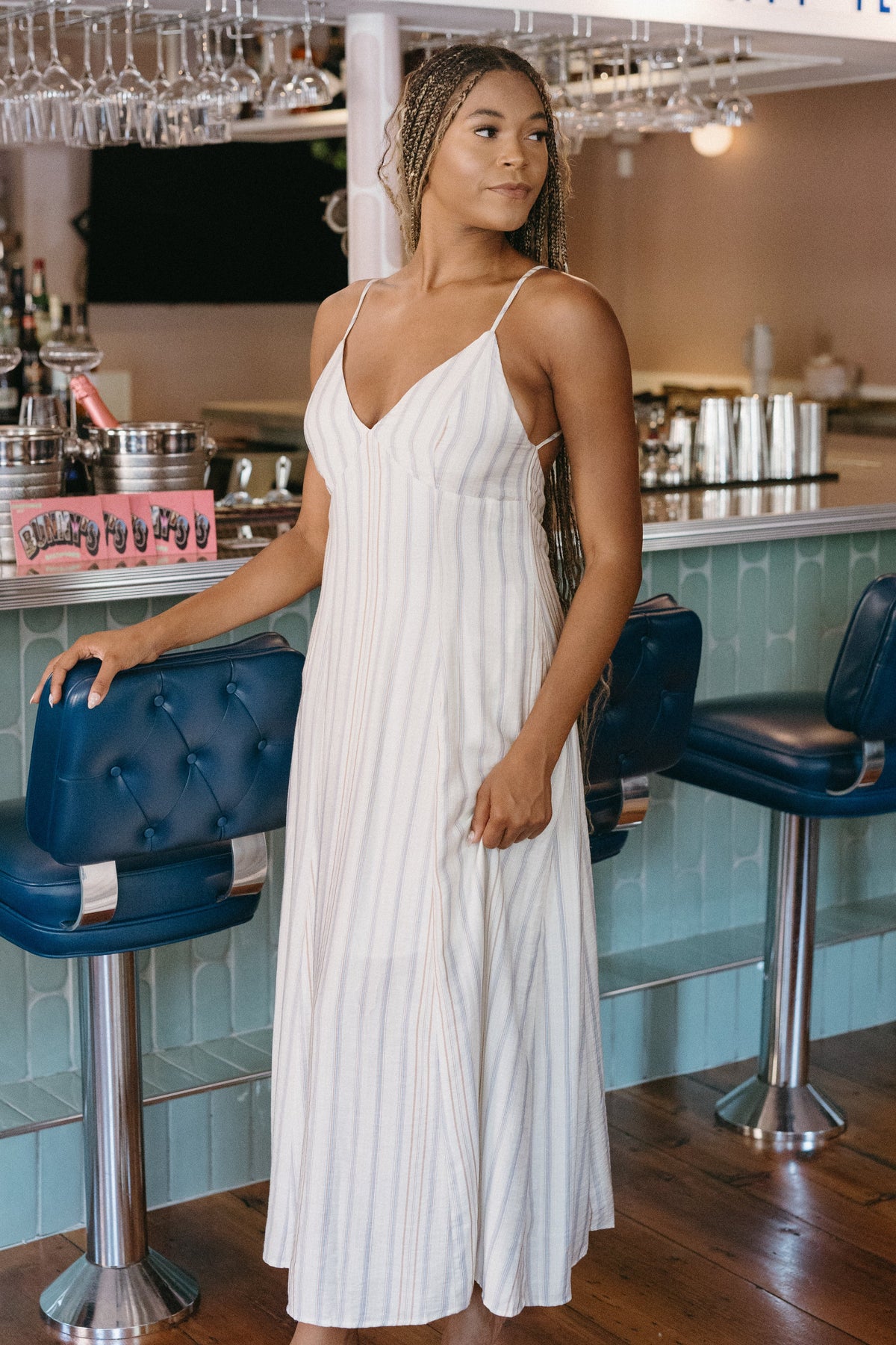 Woman in a white dress standing in a bar with blue stools and a counter.