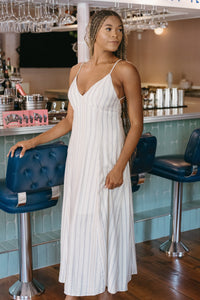 Woman in a white dress standing in a bar with blue stools and a counter.