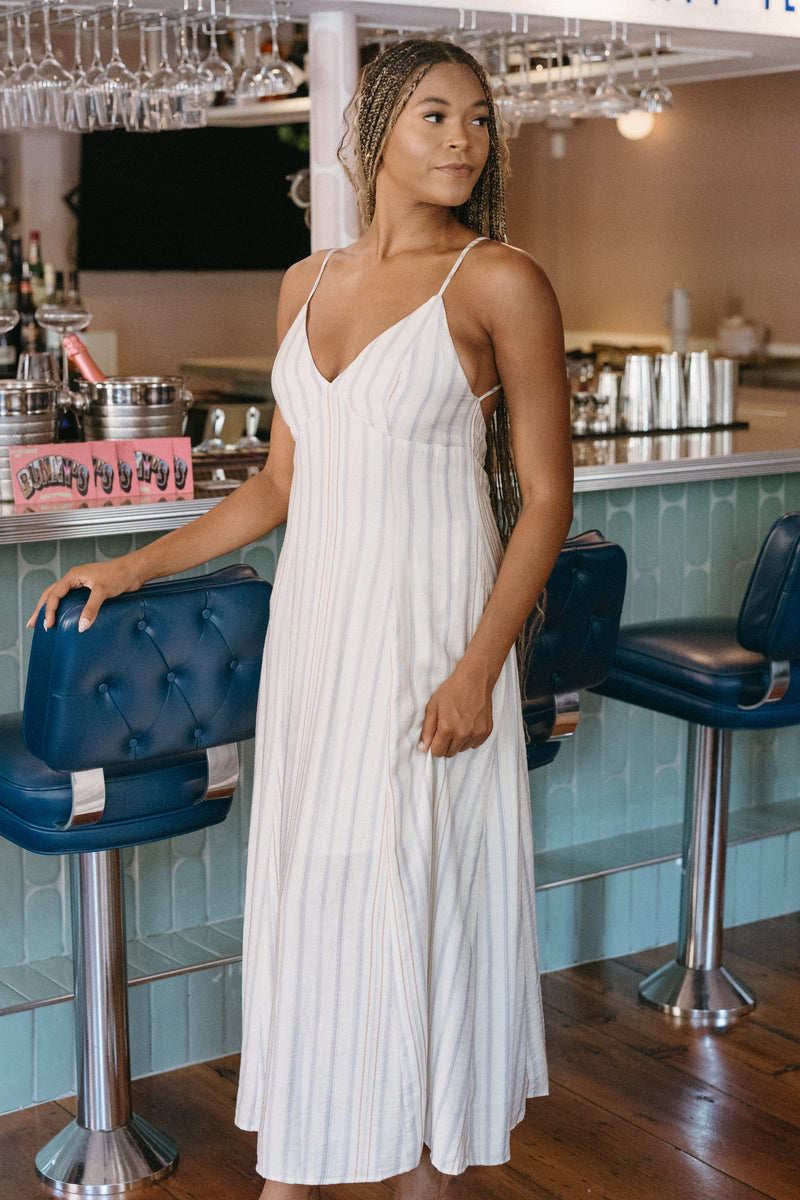 Woman in a white dress standing in a bar with blue stools and a counter.