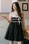 Woman in a black and white dress standing in a restaurant with patterned wallpaper.