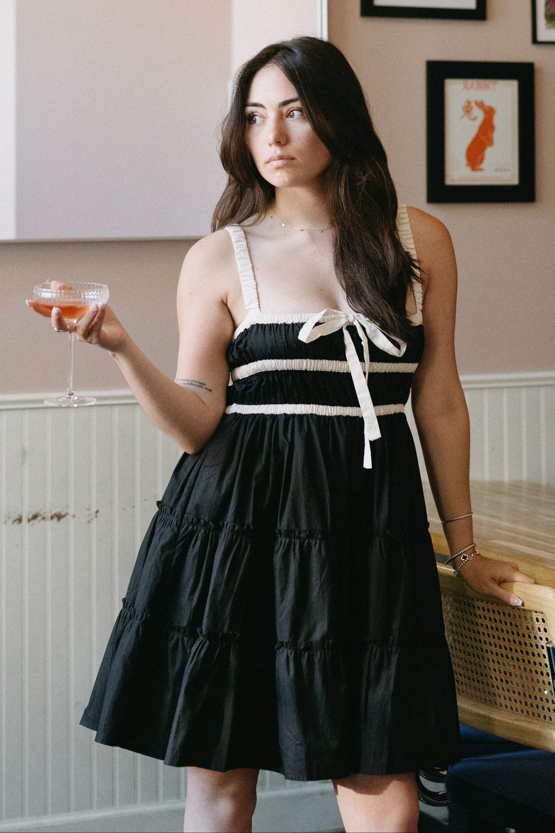 Woman in a black and white dress standing in a restaurant with patterned wallpaper.