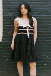 Woman wearing a black dress with white accents against a dark brick wall.