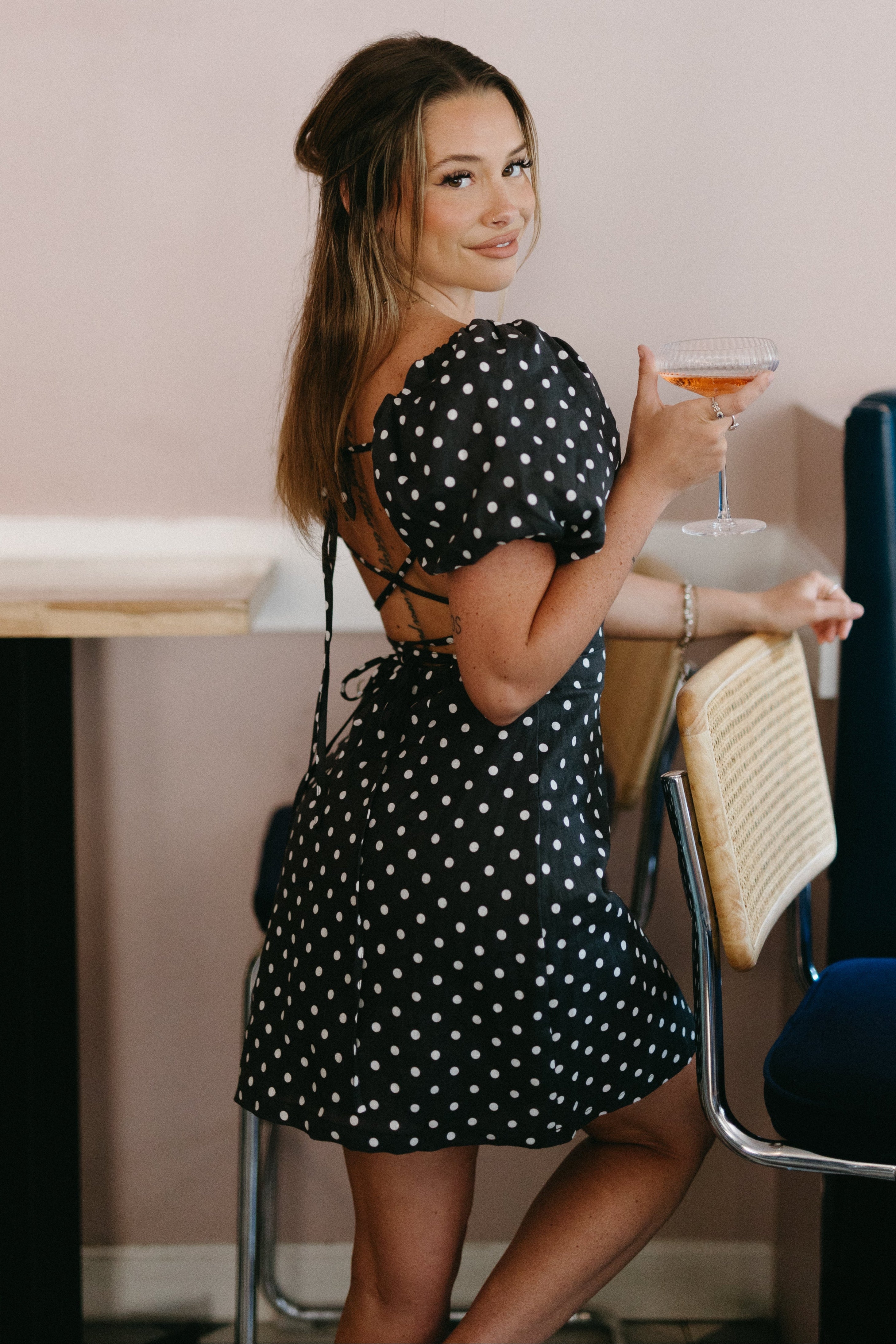 Woman in a polka dot dress holding a drink in an indoor setting