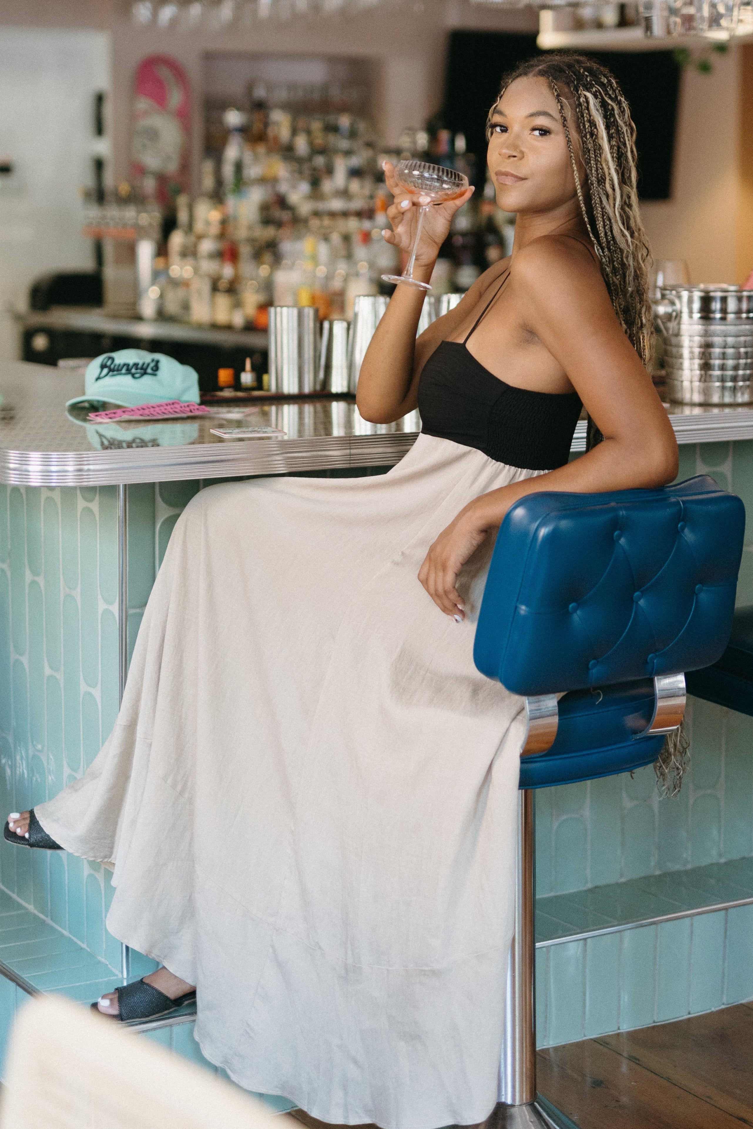 Woman sitting at a bar with 'Summer Vibes and Bubbly Delights' sign above.