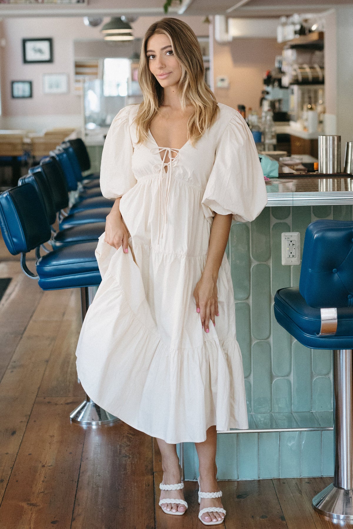 Woman in a white dress standing in a modern cafe with blue chairs and a 'Summer Bubbly' sign.